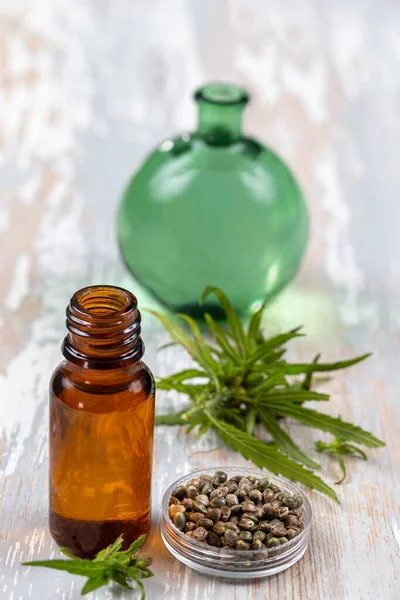Ekologisk hampa vegetabilisk olja med blad och frön tefat, trä bakgrund — Stockfoto