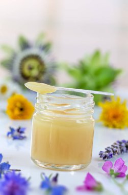 Kraliyet jölesi kaşığı dolu, açık dikey arkaplanda çiçeklerle benekli..