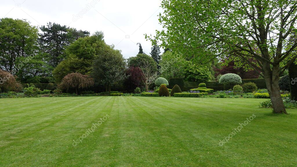Scenic View of a Beautiful English Style Landscape Garden with a Green Freshly Mowed Lawn, Colourful Flower Beds and Green Plants 