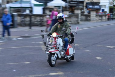 Bath, İngiltere - 19 Ekim 2014: Adam şehir merkezinde bir caddede modifiye edilmiş bir Vespa 'ya biniyor. Somerset ilçesindeki tarihi kent her yıl 4 milyondan fazla ziyaretçi alıyor..