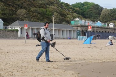 21 Mayıs 2022 'de Bournemouth, İngiltere' de bir plajda metal dedektörü kullanan bir adam. Metal detektörü, uzun zamandır kayıp olan hazineleri bulan bazı dedektörlerle birlikte popüler bir sınır çizgisi haline geldi..