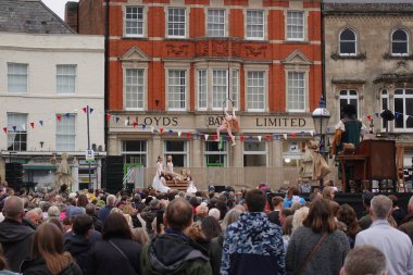 Kalabalık, 1 Mayıs 2022 'de İngiltere' nin Devizes kentinde şehir merkezindeki bir pazar meydanındaki sokak performansını izliyor..