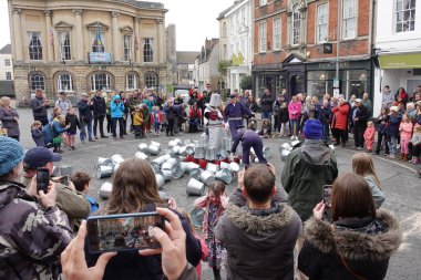 Kalabalık, 1 Mayıs 2022 'de İngiltere' nin Devizes kentinde şehir merkezindeki bir pazar meydanındaki sokak performansını izliyor..