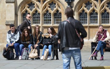 Onlookers watch as a musician performs outside Bath Abbey and the Roman Baths on May 3, 2016 in Bath, UK. Somerset city is a popular travel destination with 4 million tourist visits each year.