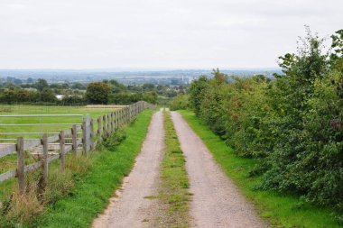 Yol boyunca çitleri ve bulutlu gökyüzü olan güzel bir kırsal yol manzarası.