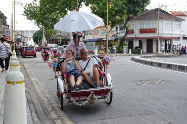 George Town, Malezya - 24 Nisan 2019: Eski şehir merkezinde halka açık bir bisiklet taksisine binen yolcu.