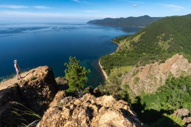 Bir kız dik bir uçurumun tepesinde duruyor ve Baykal Gölü 'ne hayran.