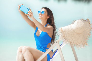 Yazın sahilde cep telefonu olan bir kadın. Bayan telefonda konuşuyor. Kadın akıllı telefonuyla fotoğraf çekiyor..