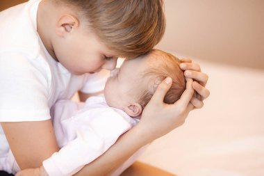 Küçük erkek kardeş yeni doğmuş kız kardeşini tutuyor. Bebek ve çocuk içeride..