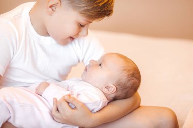 Küçük erkek kardeş yeni doğmuş kız kardeşini tutuyor. Bebek ve çocuk içeride..