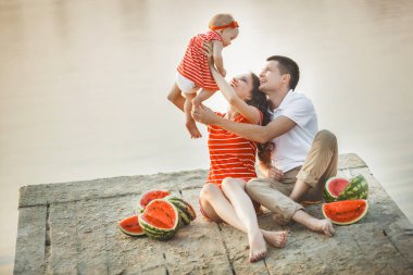 Genç bir aile dışarıda. Suya yakın insanlar. Anne ve baba kumsalda bebekleriyle..