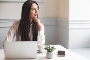 Kafeteryada dizüstü bilgisayarla yazı yazan çekici genç bir kadın. Esmer, içeride, aletlerle..