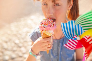 Yazın arka planda dondurma yiyen tatlı bir kız. Dondurma yiyen kızıl saçlı küçük kızın yakın plan portresi..