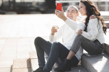 Genç, çok ırklı bir çift cep telefonuyla selfie çekiyor. Erkek ve kadın birlikte eğleniyor. Gençler akıllı telefonda konuşuyor..