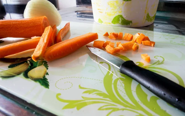 Raw carrots chopped into small pieces and into strips with onion and knife photographed from above