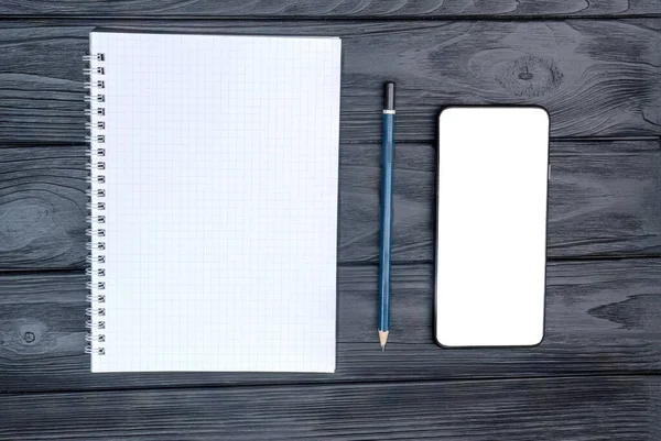 Top view of a notebook with a pencil and a blank smartphone against a dark background. . High quality photo