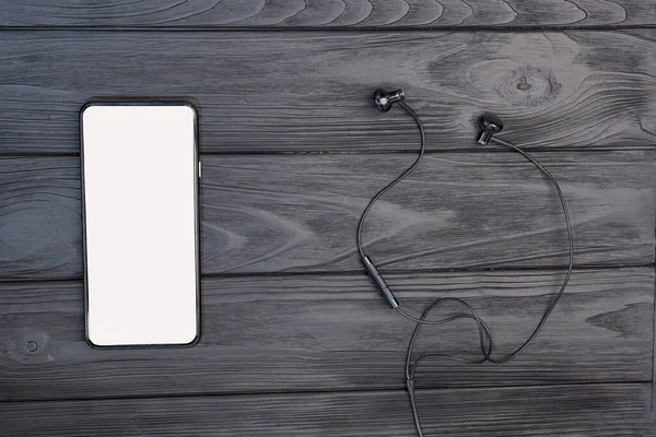 Top view of an empty smartphone and wired headphones. on a wooden background. White empty space for advertise text. High quality photo