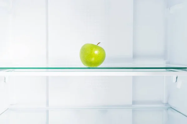 green apple on a glass shelf in the refrigerator