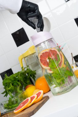 Şef, siyah beyaz bir mutfağın arka planına greyfurt ve nane şekerinden yapılmış meyve suyu ile buz ekler.