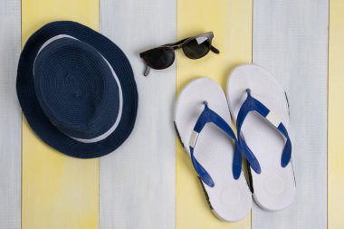 Gri-sarı bir yüzey, plaj terlikleri, güneş gözlükleri ve bir şapka