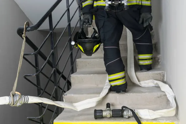 on a smoke-free staircase, a firefighter holds a helmet with a flashlight in his hands, against the background of special equipment a barrel and a hose for water supply