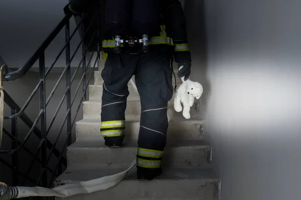 Egy Tűzoltó Mászik Fel Lépcsőn Sötétben Kezében Egy Gyerekjátékkal — Stock Fotó