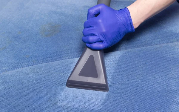 stock image hand in a protective glove, collecting dirt from a blue sofa, using a washing vacuum cleaner, close-up