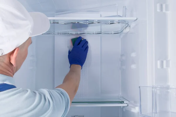 cleaning service worker wipes refrigerator shelves with a sponge with cleaning foam