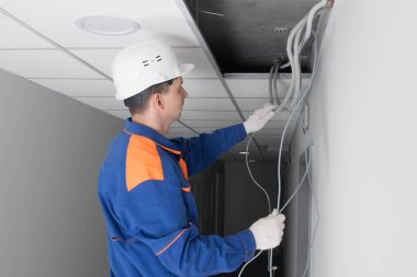 Elektrikçi asılmış tavanda gizlenmiş iletişimdeki bir arızayı düzeltiyor.