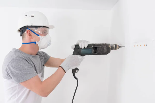 防護ヘルメットとマスクのビルダーは パンチャーで 家具を固定するための壁に穴を開けます — ストック写真