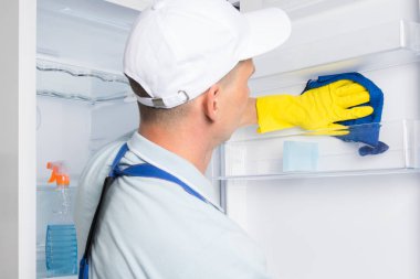 İşçi dezenfekte eder ve buzdolabının kapısını yıkar.