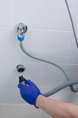 Bir çamaşır makinesi kurulumu, su ve kanalizasyon bağlantısı, yakın plan, koruyucu eldiven.