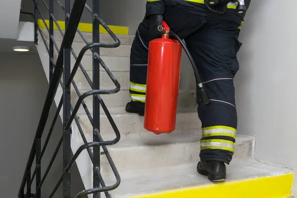 内部の脱出階段に沿って消火器で登る消防士のリアビュー — ストック写真