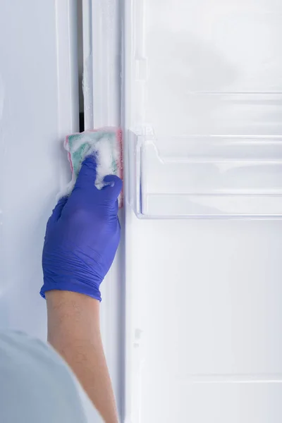 the hand of a cleaning service worker in a protective glove wipes the refrigerator with a sponge with cleaning foam