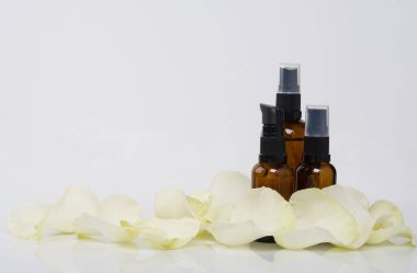 Beyaz arka planda, bir yazı için yeri olan, üç şişe masaj yağı, gül yapraklarıyla çevrili.