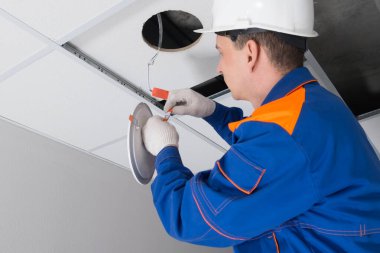 Yakın plan, mavi üniformalı ustabaşı yanlış tavan ışıklandırması, lamba bağlantı kutusu bağlantılarını kontrol ediyor.