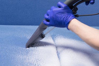 Mavi bir kanepeden toprak toplamak için elektrikli süpürge ve köpük kullanıyoruz. Yakın plan.