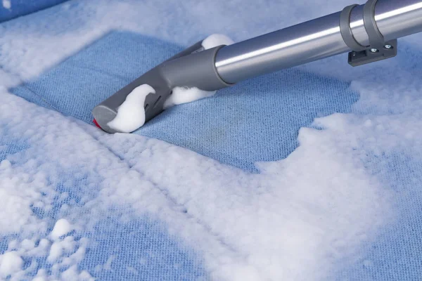 Kirli bir kanepenin mavi kumaşından, elektrikli süpürge kalın köpük toplar.