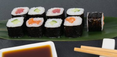 Masanın üzerinde, bambu yaprağının üzerinde, balık ve sebzelerle dolu renkli rulo, soya sosu ve yemek çubukları, her şeyin yakın çekimi.