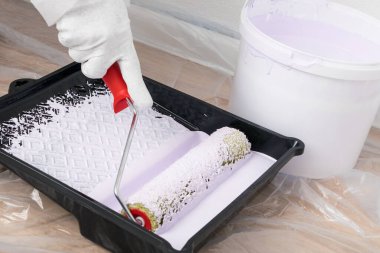 Duvarları mora boyamak için bir silindir tutan el.