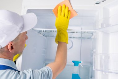 Bir işçi buzdolabının içindeki rafları paçavrayla yıkıyor.