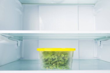 Konteynırdaki yeşil fasulyeler boş bir buzdolabının rafında.