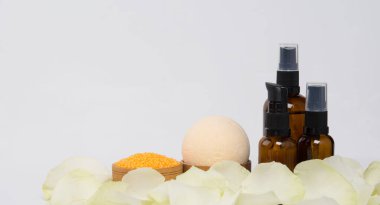 Beyaz bir arka planda, bir yazı için yeri olan, üç şişe masaj yağı, gül yaprakları ve banyo tuzu ile çevrili.