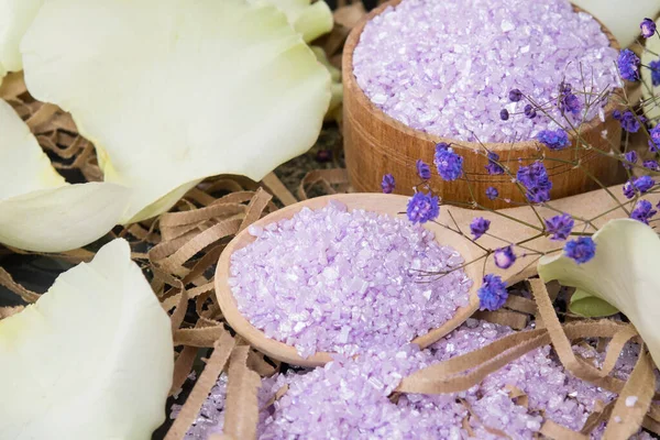 Gül yaprakları ve çiçeklerle çevrili parçalanmış mor banyo tuzu.