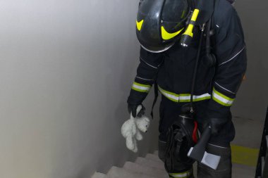 Bir itfaiyeci elinde oyuncak bir oyuncak ve elinde kapı açmak için baltayla merdivenleri tırmanır.