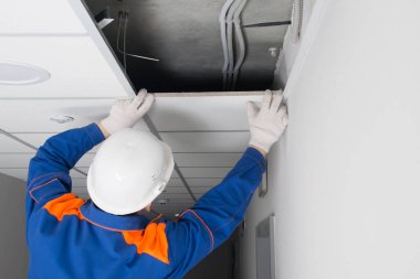 Askıya alınmış tavanların kurulumu ustası, metal bir çerçeve ve dikiz aynasındaki plakaların montajını tamamlar