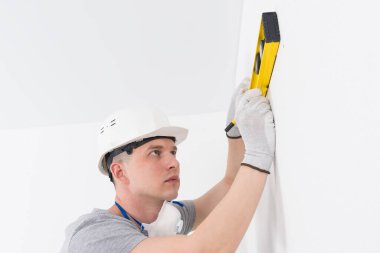 Beyaz miğferli bir müteahhit, bir seviyenin yardımıyla, deliğin altındaki bir yeri işaretliyor.