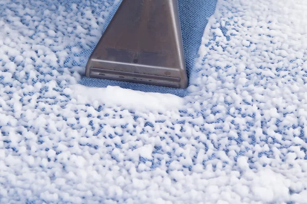 close-up of a washing vacuum cleaner picking up dirty foam from the fabric of the sofa