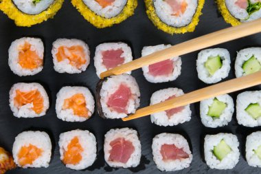 Siyah bir masada, somon, ton balığı ve salatalıkla sıralanmış, ahşap çubuklar bir tane alır.