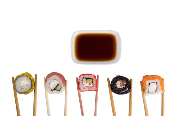 白いテーブルの上には マグロ サーモン ソフトチーズの5つのロールが並べられ 天ぷらで焼いたものは木の棒を持ち 醤油は容器の上に盛り付けられている — ストック写真